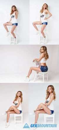 Sexy Blond Female in a White T Shirt and Denim Shorts Posing on a Chair in a Studio